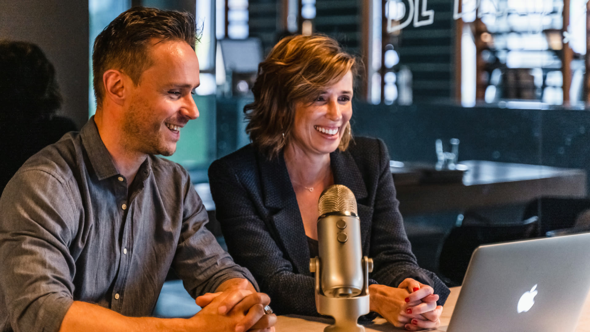 Two SkillsGym trainers preparing a live session at a table with a microphone and a laptop